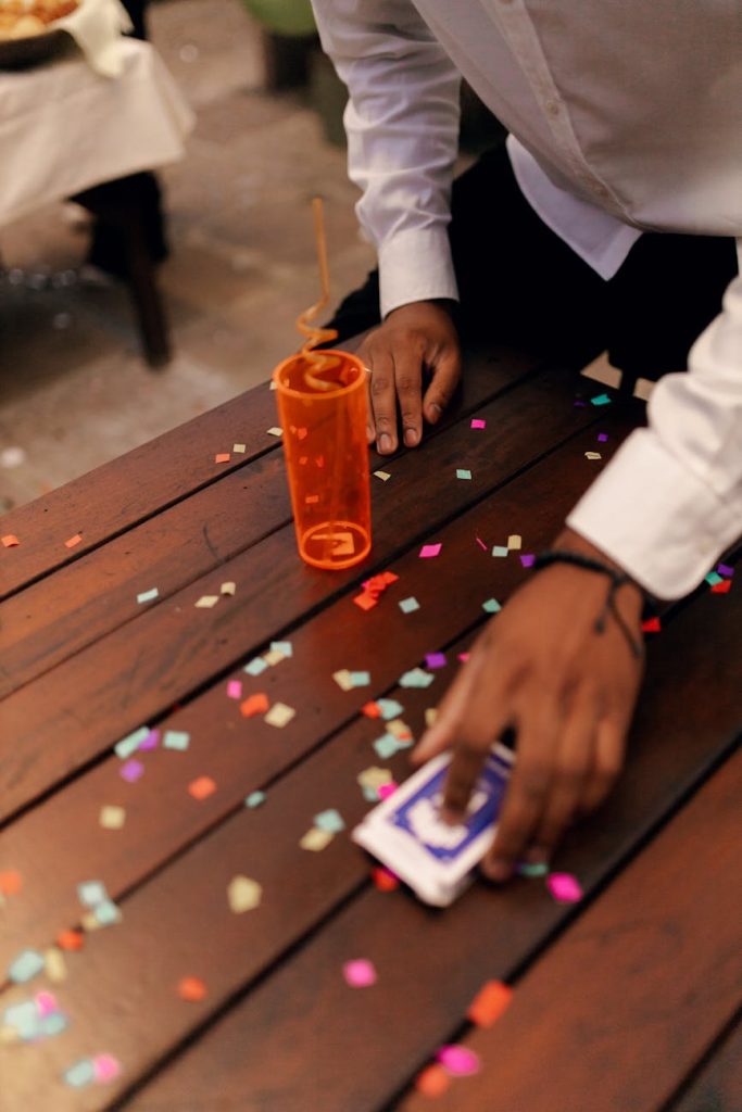 A person tidying confetti off a wooden table at a festive celebration, party setting.